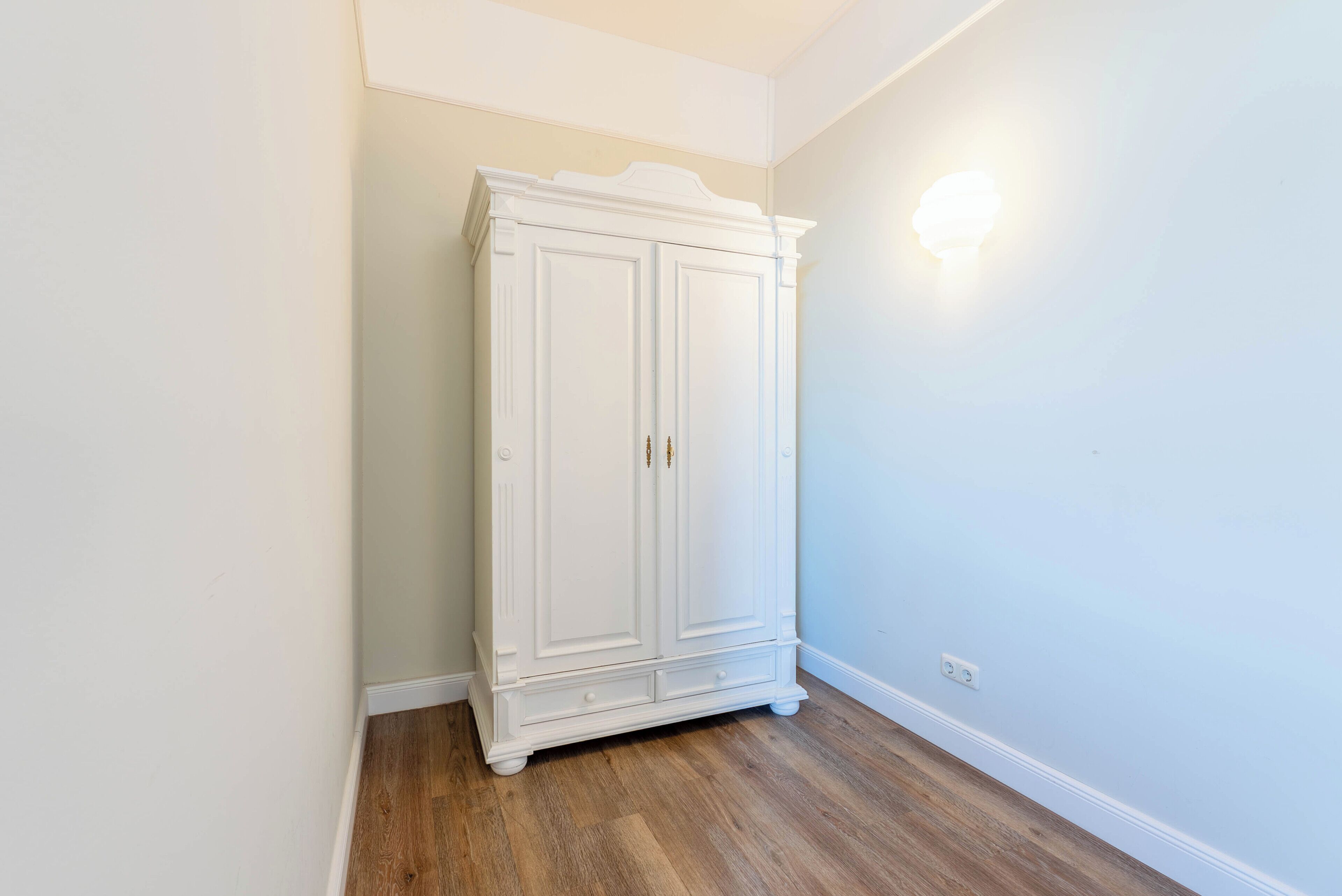 A white wardrobe in a corner with a light switch on the wall.