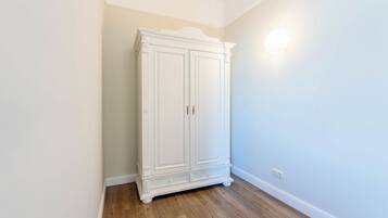 A white wardrobe in a corner with a light switch on the wall.
