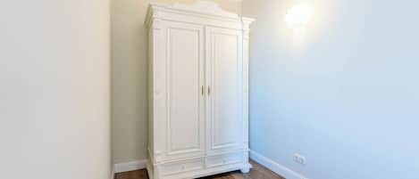A white wardrobe in a corner with a light switch on the wall.