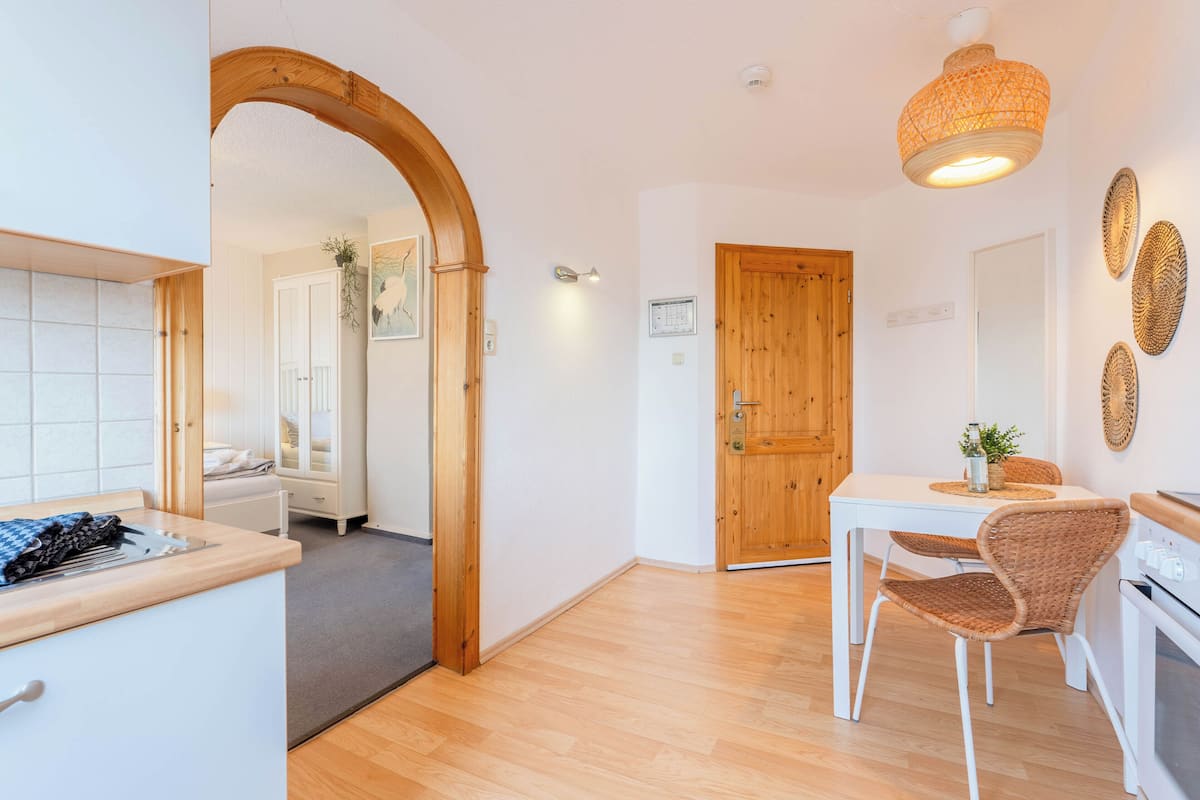 A modern kitchen with wooden flooring, a dining area with wicker chairs, and a wooden door.