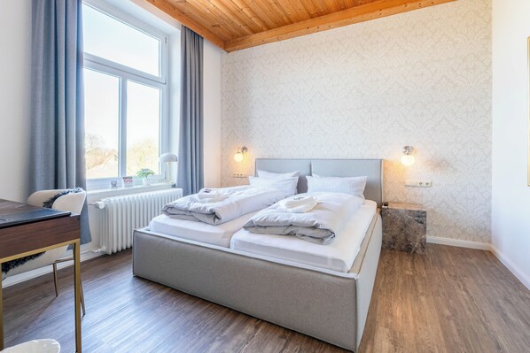 A bedroom with a bed, a desk, a window with curtains, and a radiator.