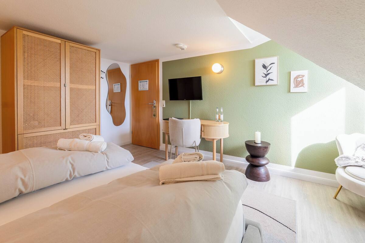 A hotel room with two beds, a TV, a desk with a chair, and artwork on the wall.