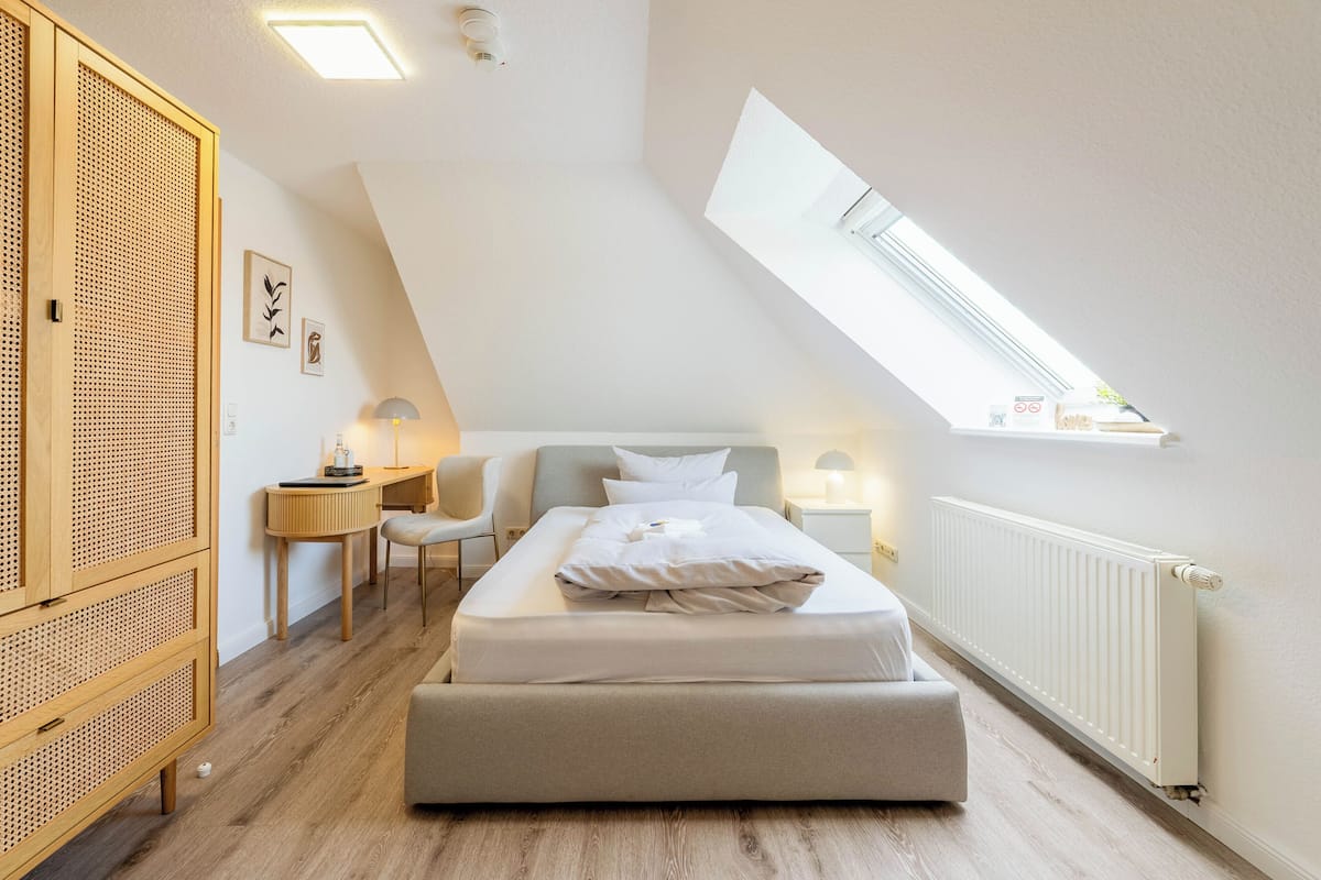 A bedroom with a loft bed, a desk, a chair, a lamp, and a window.
