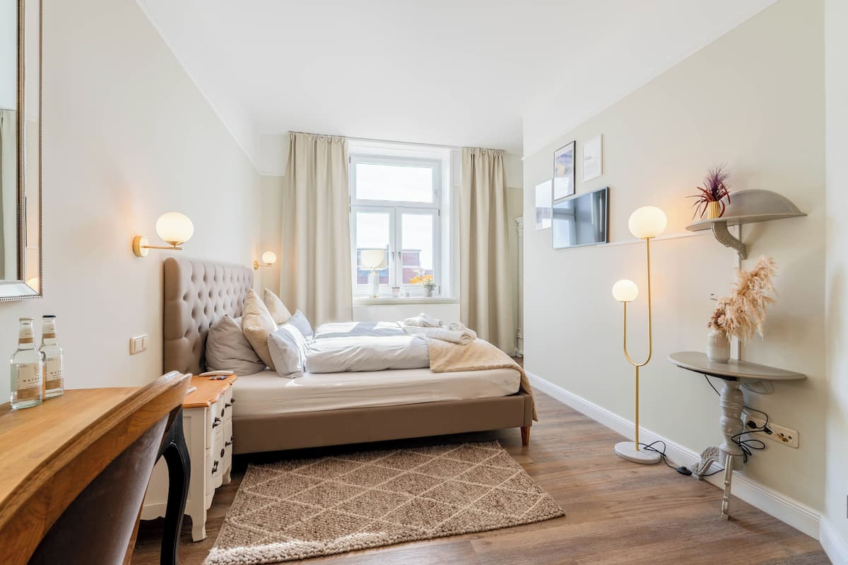 A bedroom with a bed, bedside table, lamp, and a window with curtains.