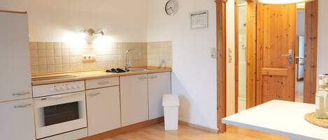 A kitchen with a stove, oven, sink, and a wooden door leading to another room.