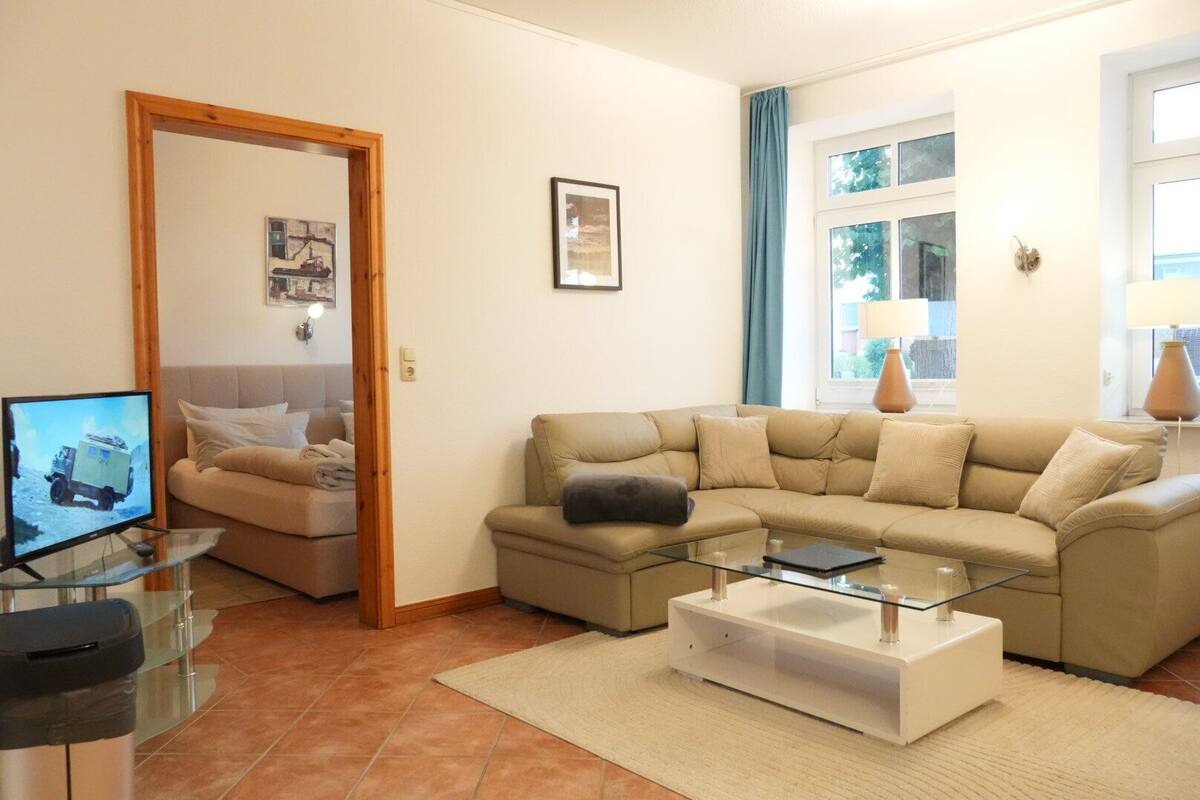 A living room with a sofa, a glass coffee table, a television, and a door leading to another room.