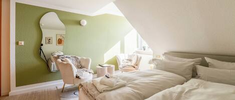 A bedroom with a bed, two chairs, a mirror, and a green wall.