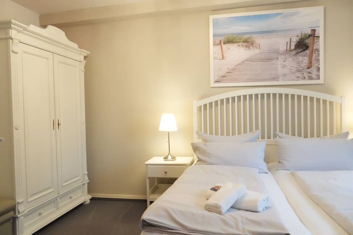 A hotel room with a bed, a nightstand with a lamp, a wardrobe, and a beach-themed painting on the wall.