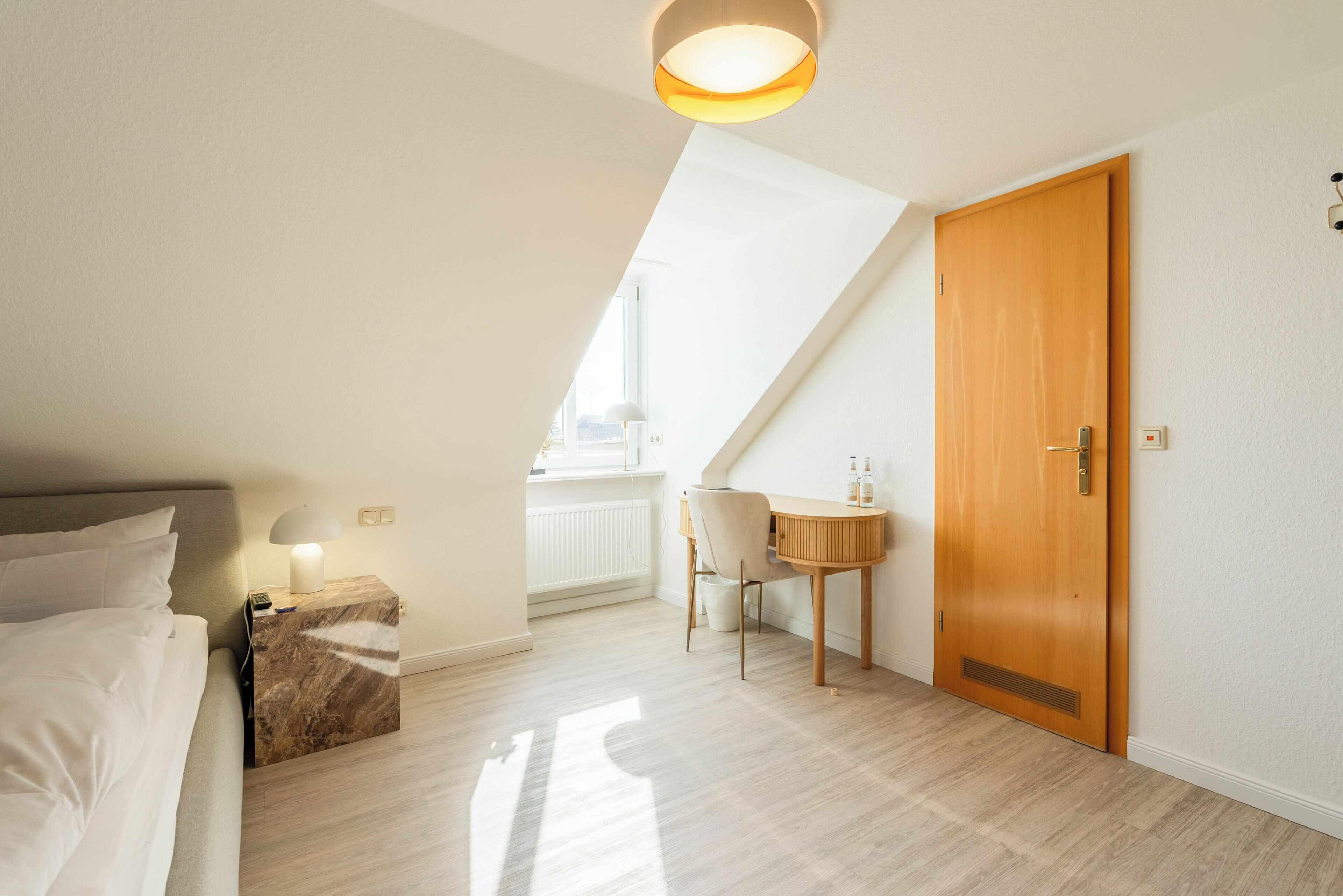 A bedroom with a bed, a nightstand, a desk, and a door.