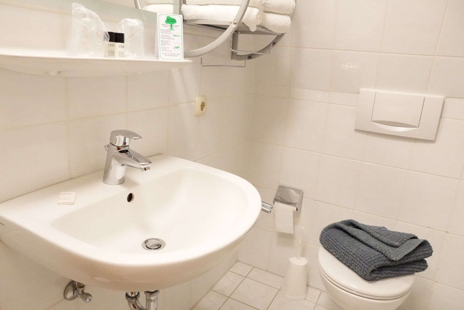 A bathroom with a white sink, a toilet, a towel rack with towels, and a soap dispenser.
