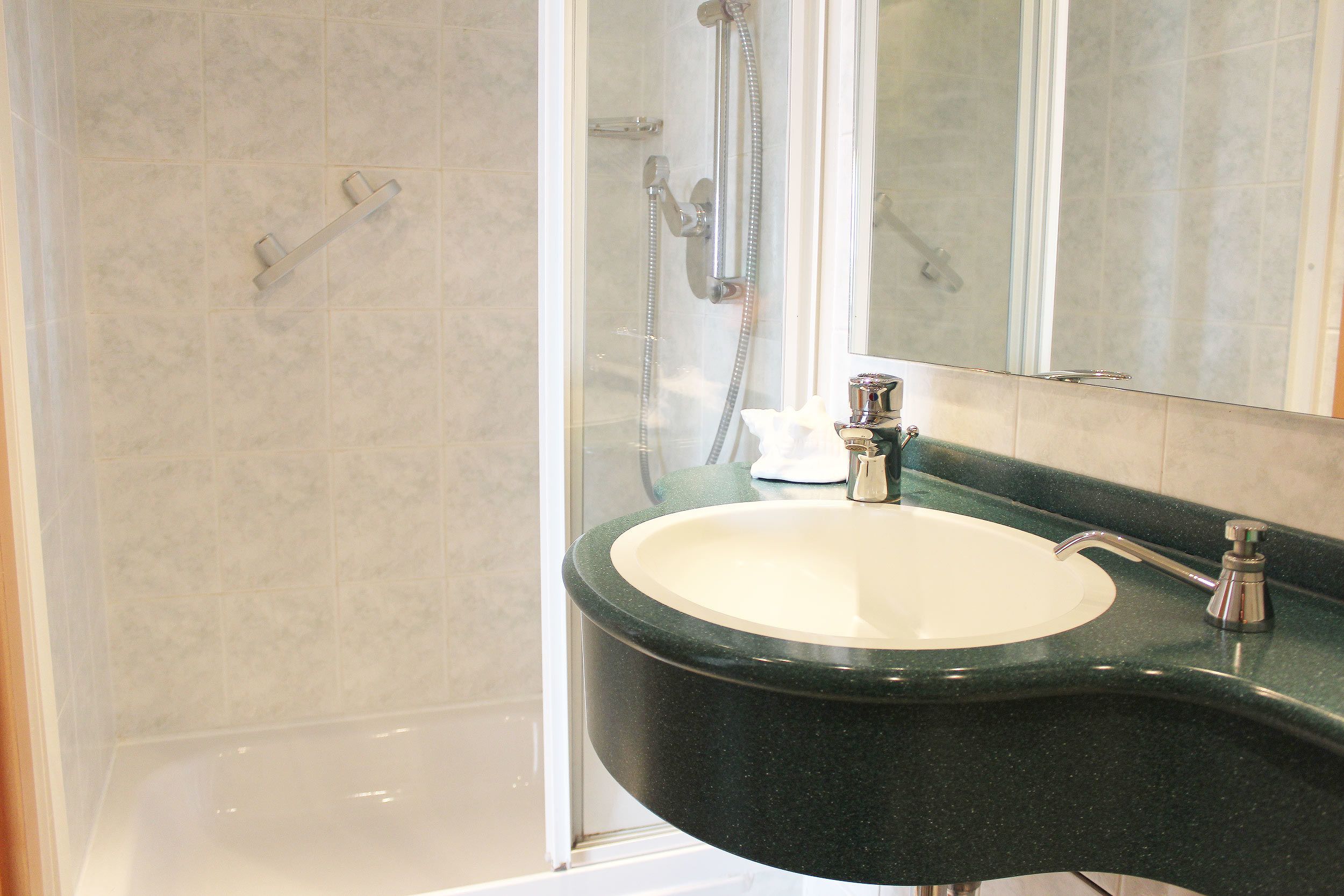 Un baño con bañera, lavabo con encimera verde y ducha con puerta de cristal.