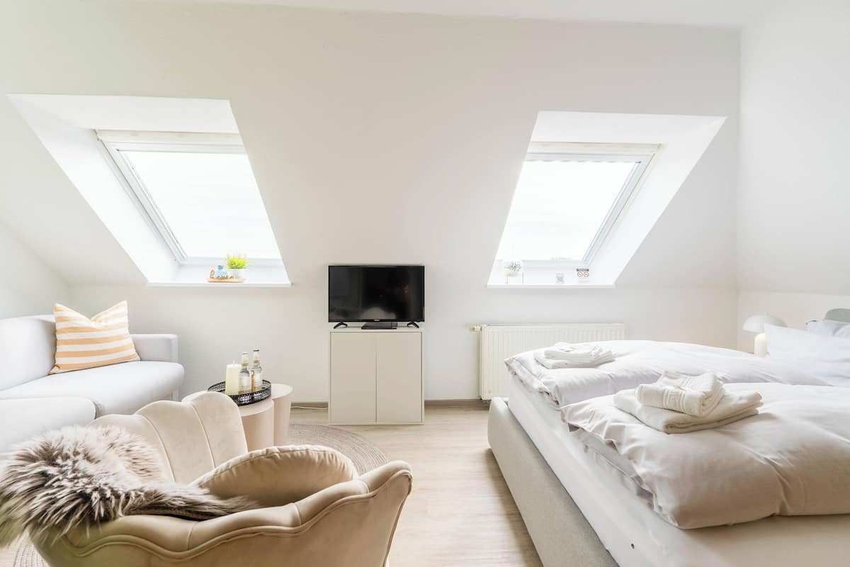 A modern bedroom with a TV, two windows, a sofa, a chair, and a bed.