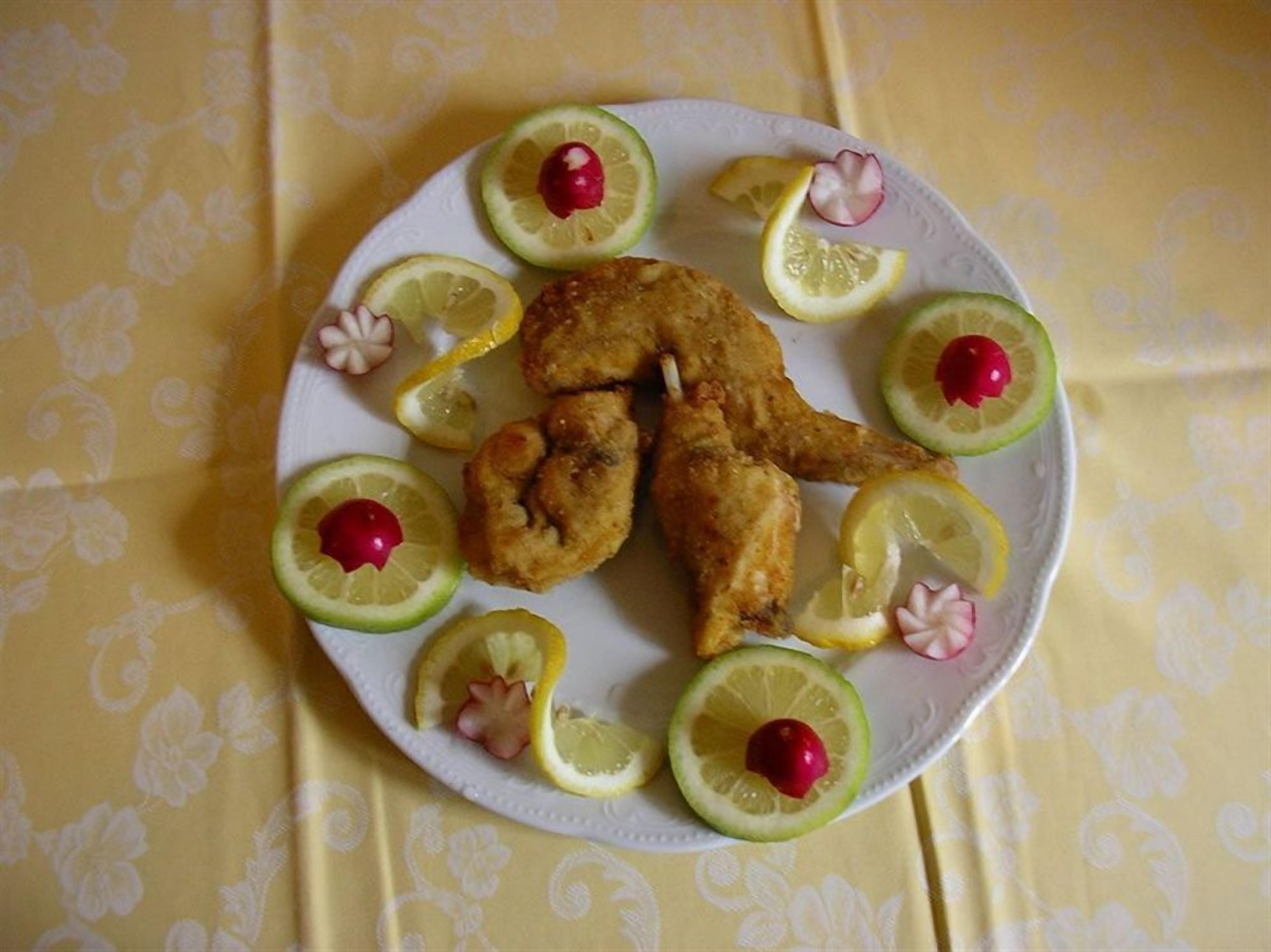 A plate with fried chicken and lemon slices garnished with radishes and cherry tomatoes.