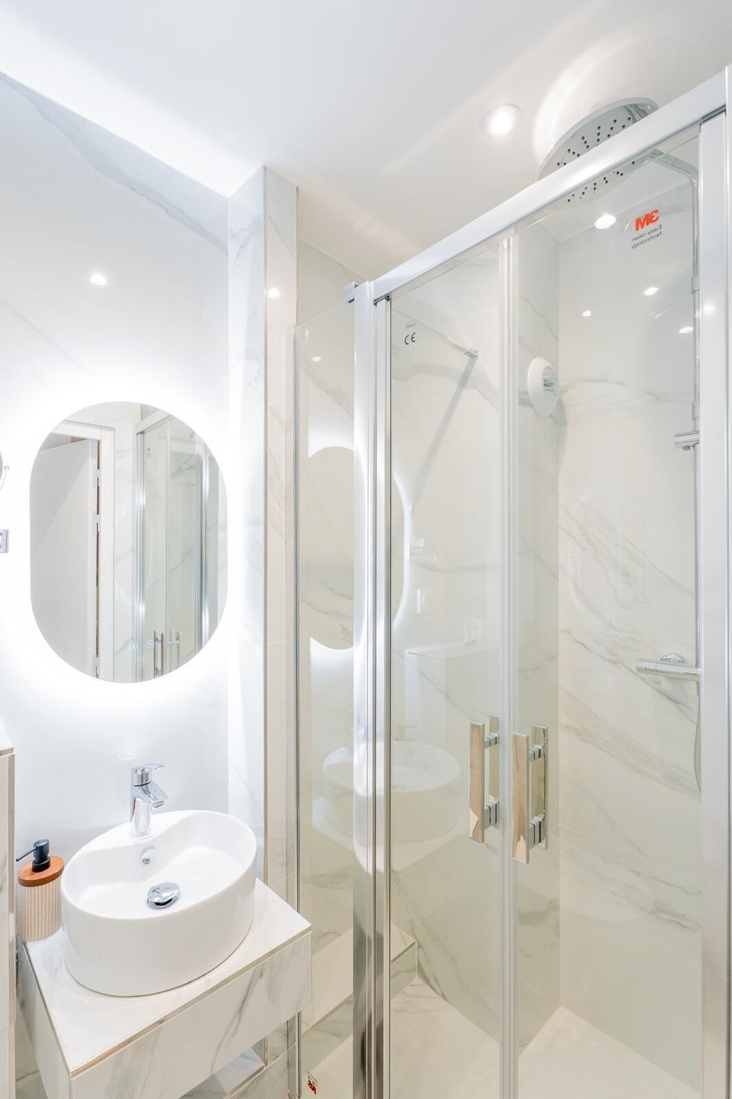 Un baño moderno con ducha envuelta en vidrio, un espejo redondo y un lavabo blanco.