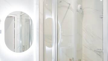 A modern bathroom with a glass-enclosed shower, a round mirror, and a white sink.