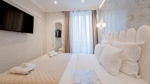 A hotel room with a large bed, a flat-screen TV mounted on the wall, and a view of the city through the window. - Garbo hôtel (Paris)