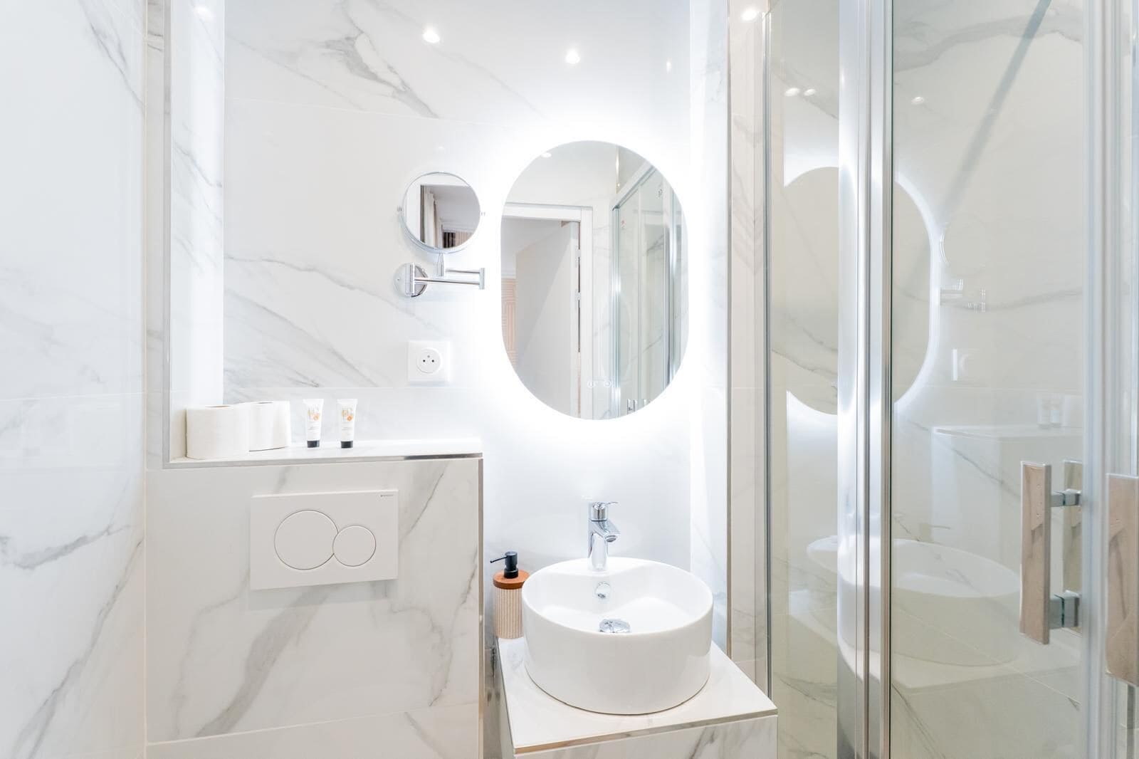 A modern bathroom with a marble vanity, a round mirror, a built-in sink, and a glass shower enclosure.