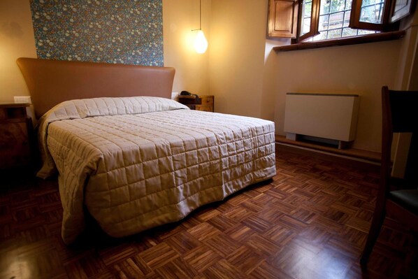 A bedroom with a bed, wooden flooring, a radiator, and a window with a view. - Hotel Diana (Lucca)