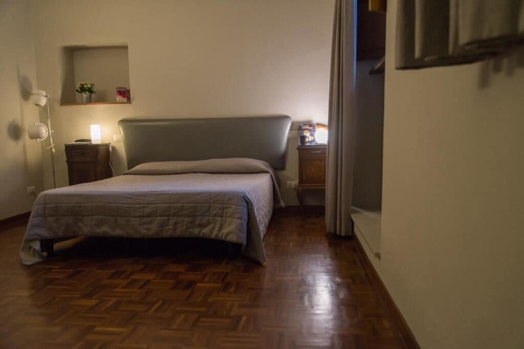 Un dormitorio con una cama, una mesita de noche, una lámpara y un pequeño estante con una planta.