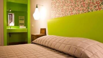 A room with a green door leading to a bathroom, a bed with a quilted cover, and a wall with a floral pattern.
