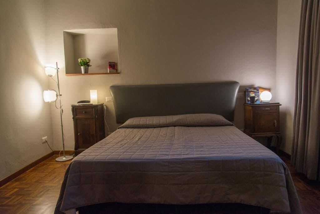 Un dormitorio ordenado con una cama, lámparas de noche, una mesita de noche y una pequeña mesa con lámpara.