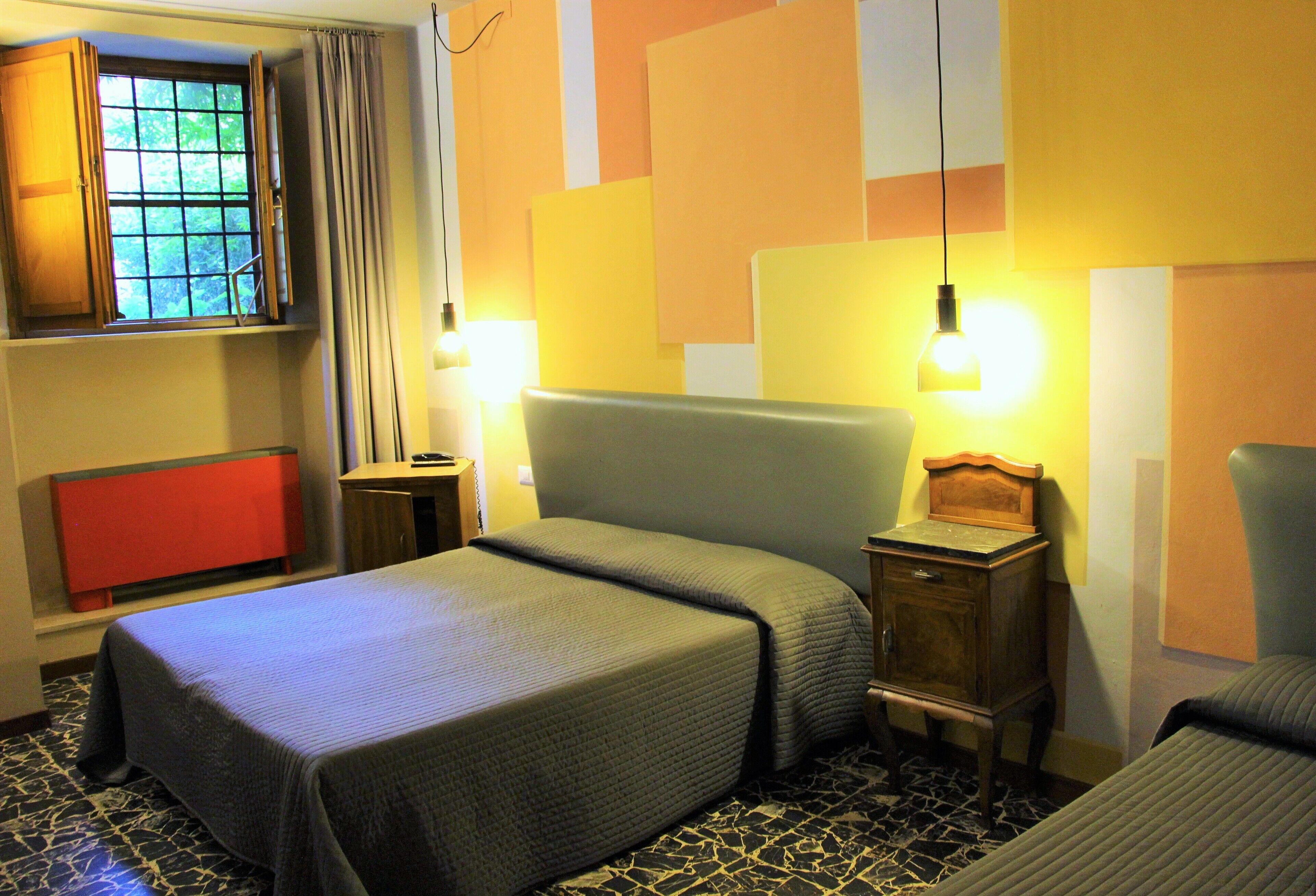 A hotel room with a bed, bedside tables, a window with curtains, and a red cabinet.