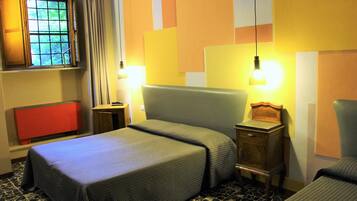 Una habitación de hotel con una cama, mesitas de noche, un ventanal con cortinas y un armario rojo.