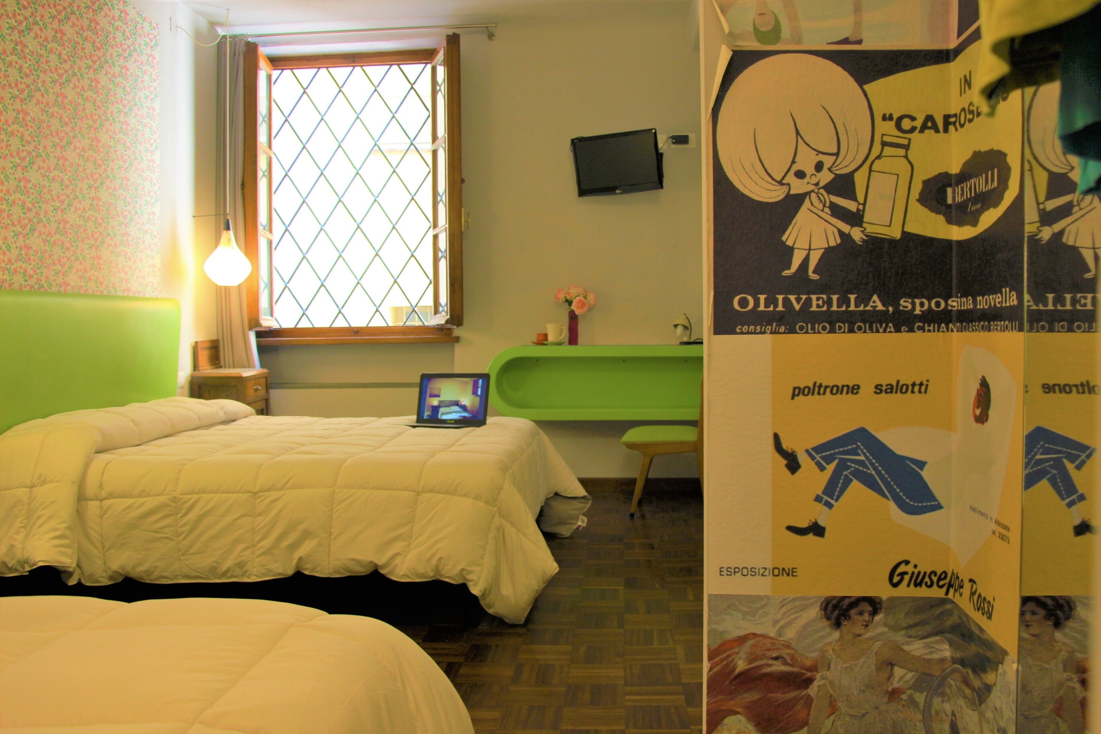 Une chambre avec deux lits, une fenêtre donnant sur un beau paysage, un fauteuil vert, une petite table avec une lampe et une affiche accrochée au mur.