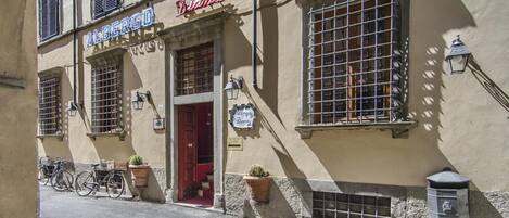 A building with a sign reading "Albergo" and "Nanna." There are bicycles parked outside and potted plants near the entrance.