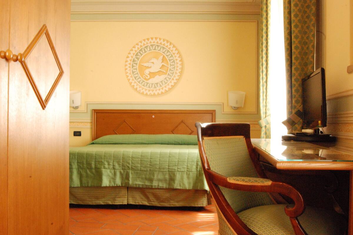 A hotel room with a bed, a chair, a television, and a decorative wall piece.
