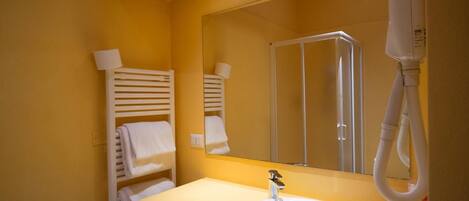 A bathroom with a white sink, a mirror, a towel rack with towels, and a handheld showerhead.