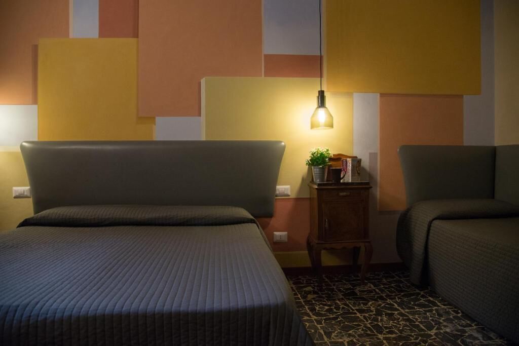 Une chambre d’hôtel avec un lit, une table de chevet, une lampe et une petite table sur laquelle est posée une plante.