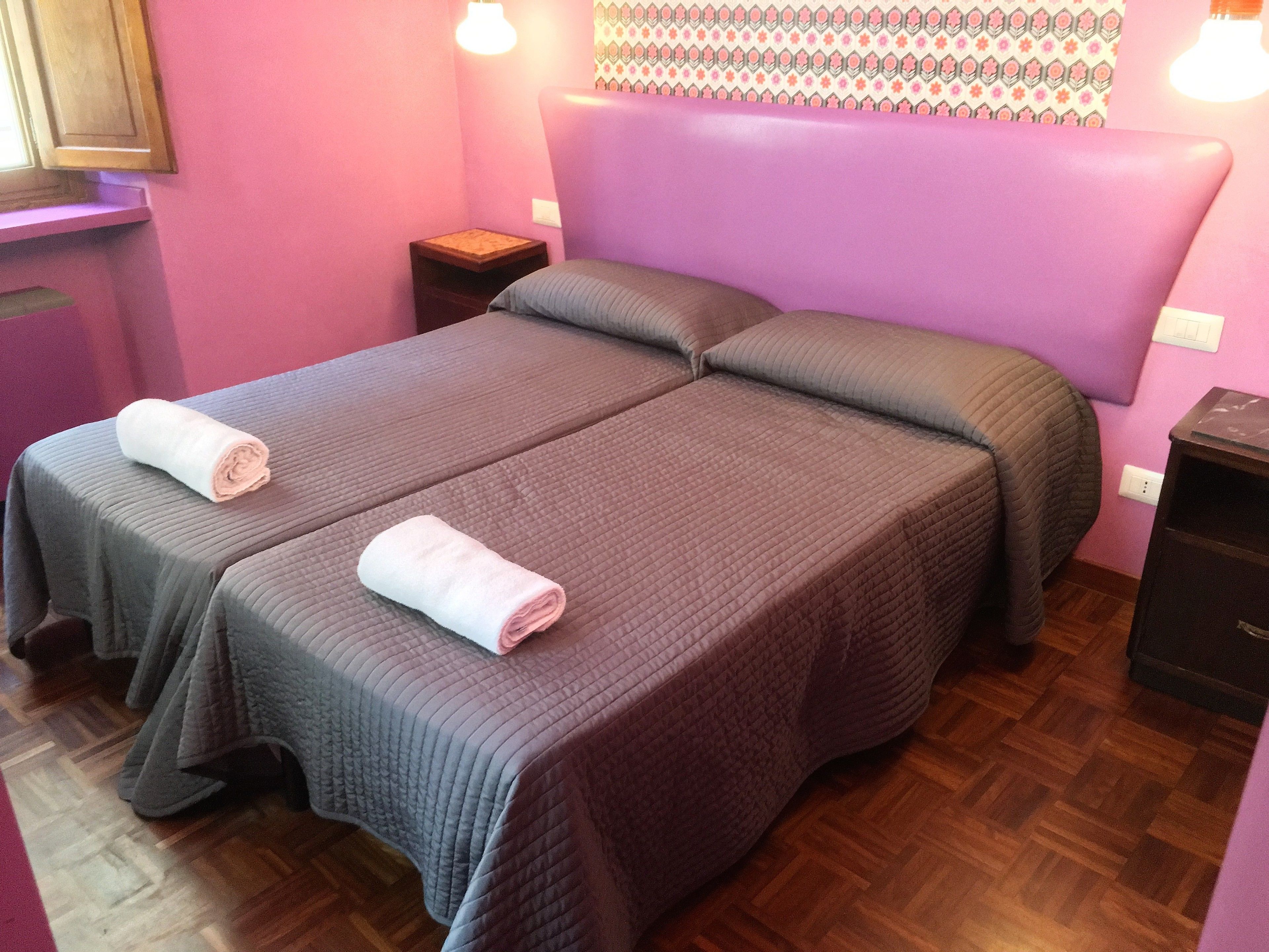Ein Doppelbett mit zwei Kissen und zwei gefalteten Handtüchern, ein Nachttisch und ein hölzernes Kopfteil.