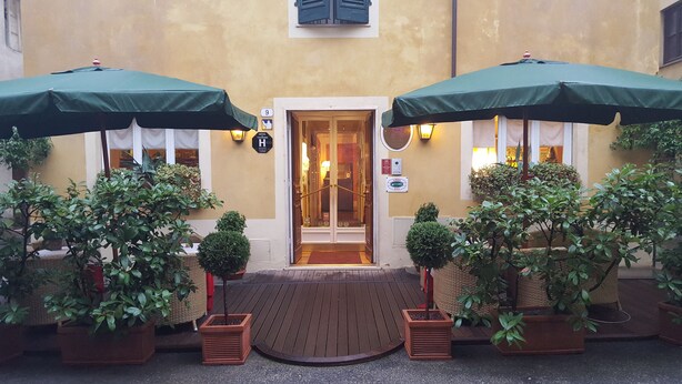 A hotel entrance with two green umbrellas, potted plants, and a wooden entrance mat. - Hotel Diana (Lucca)