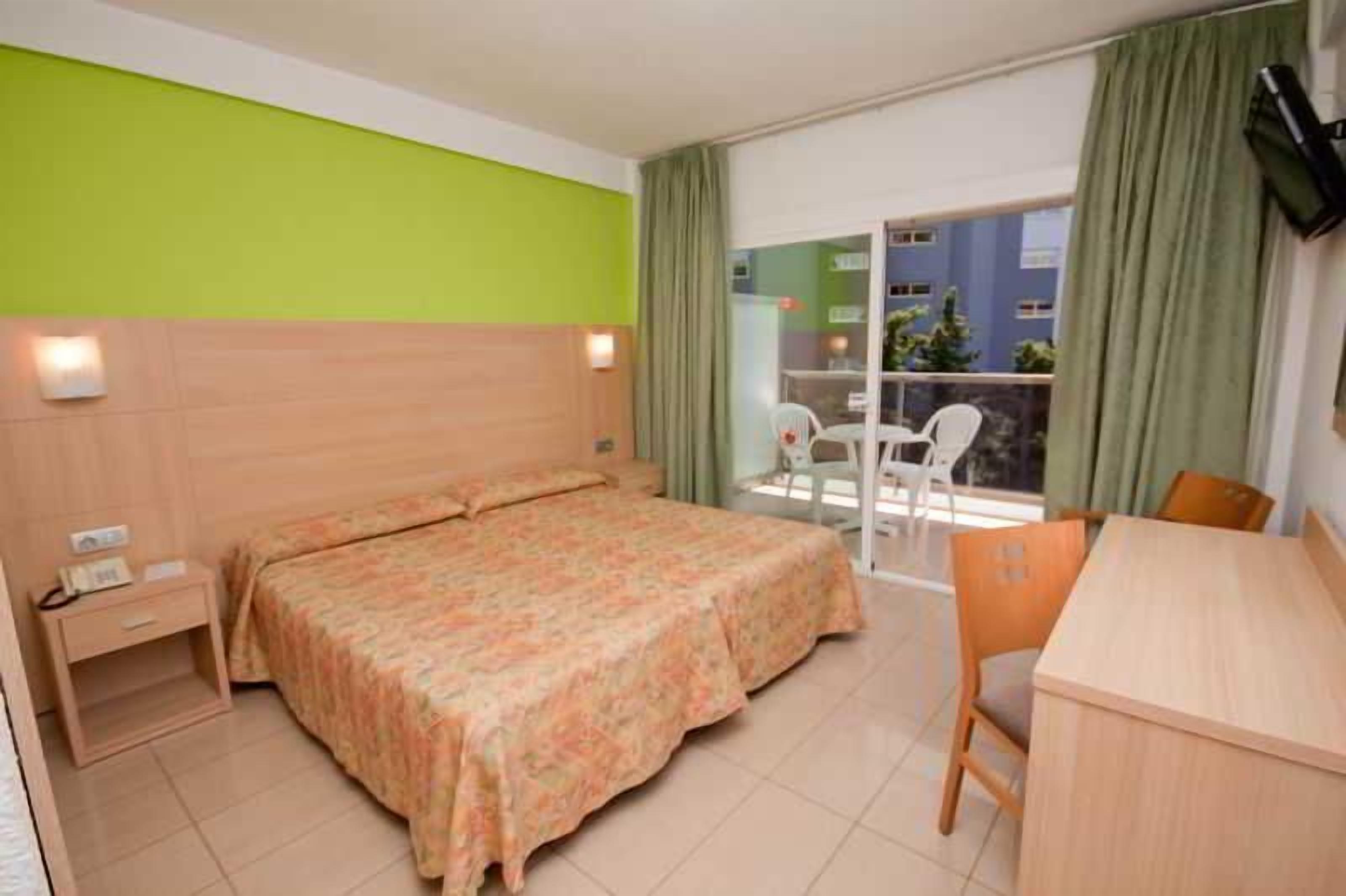 A hotel room with a bed, a desk, and a balcony with a view.