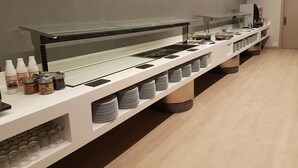 Dispositiu de buffet amb vitrina de cristall, dispensadors de condiments i plats apilats.