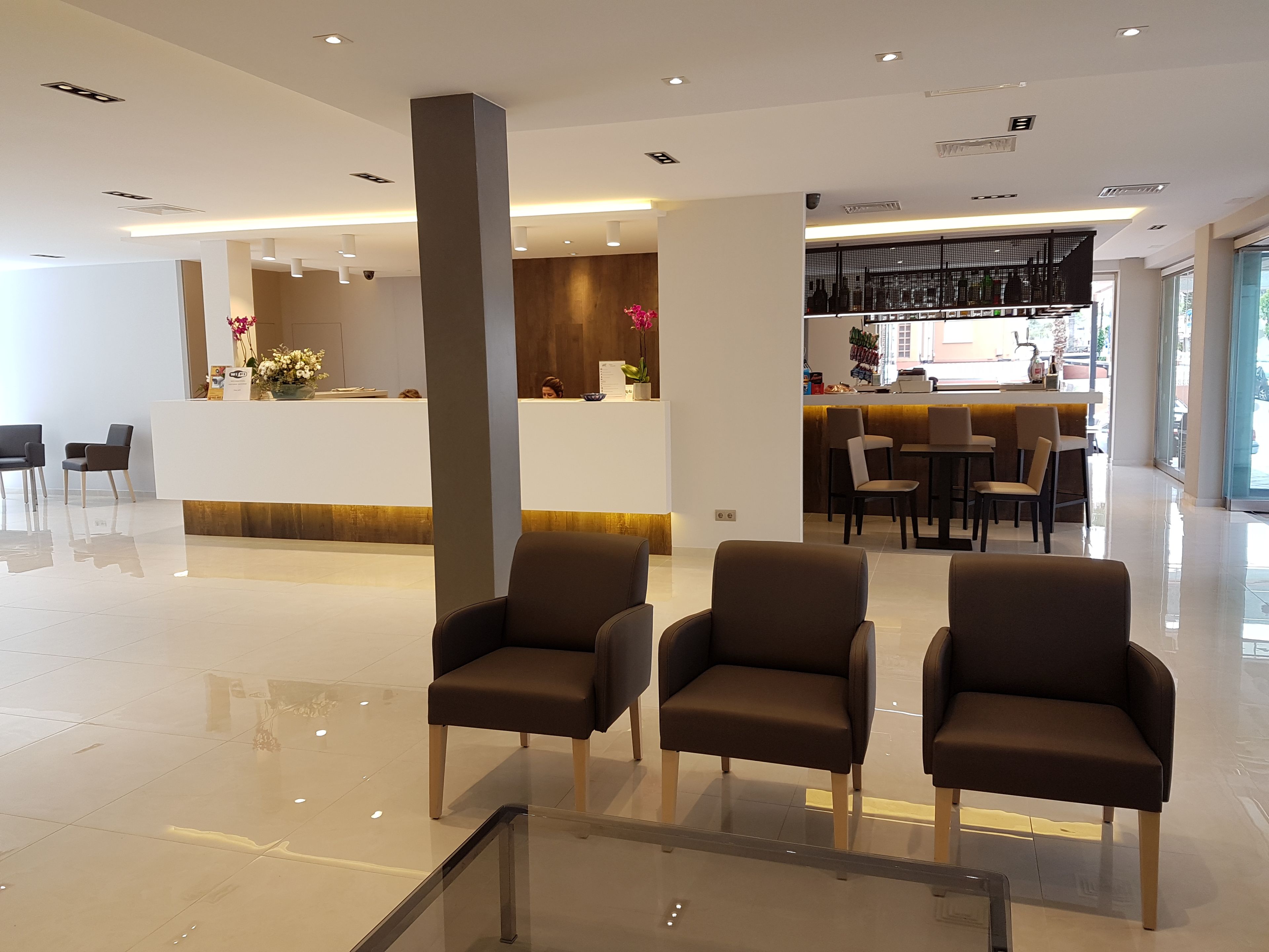 A modern hotel lobby with a reception desk, seating area, and a bar.