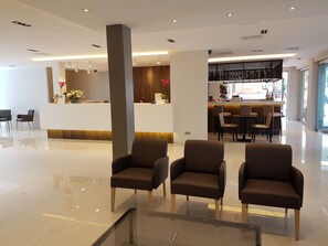 A modern hotel lobby with a reception desk, seating area, and a bar. - Hotel Perla (Benidorm)