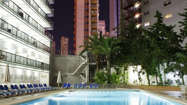 Una piscina amb gandules, una escala i un edifici amb balcons al fons.