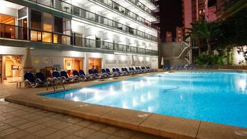 Zona de piscina de hotel con sillones de descanso y una piscina cristalina.