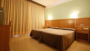 A hotel room with a double bed, a nightstand, a desk with a telephone, and a window with curtains. - Hotel Perla (Benidorm)