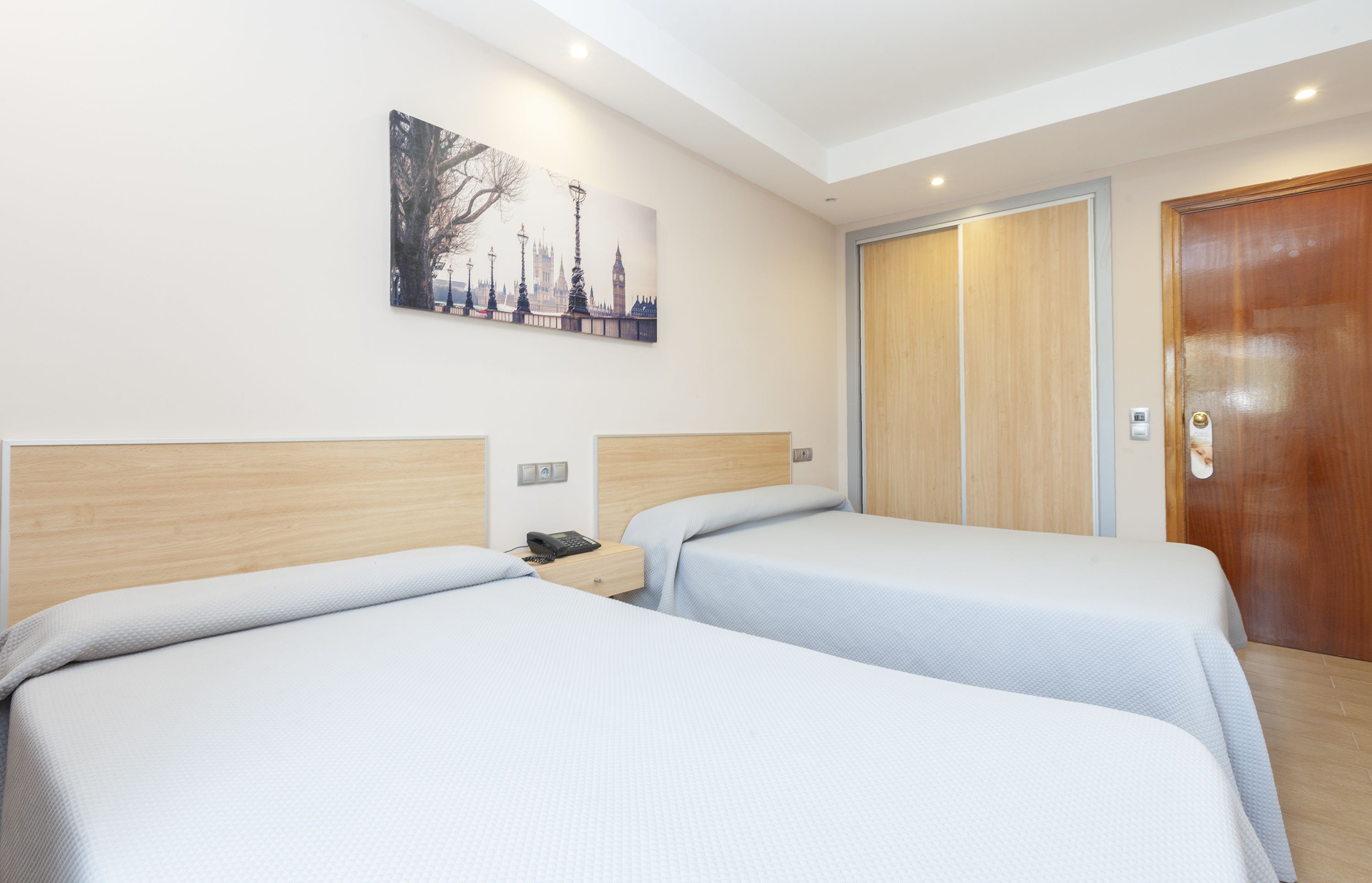 Una habitación de hotel con dos camas, una puerta de madera y un cuadro de un paisaje urbano en la pared.