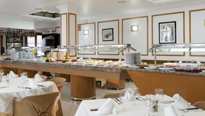 A buffet setup with multiple serving stations, a bar area with bottles, and neatly arranged tables with white tablecloths and chairs. - Hotel Olympia Ronda I (Puig)