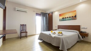 A hotel room with a bed, a desk, a chair, a painting, and an air conditioning unit. - Hotel Olympia Ronda I (Puig)