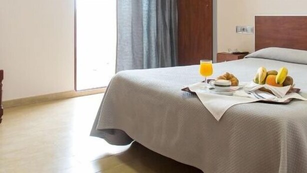 A hotel room with a bed, a bedside table with a phone, and a breakfast tray with croissants and fruit. - Hotel Olympia Ronda I (Puig)