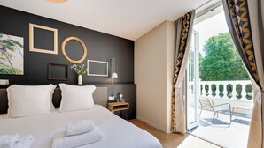 Un cuarto de hotel con una cama grande, una mesita de noche con lámpara, vista al exterior por una puerta corrediza y un balcón con una silla.