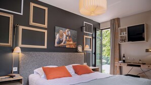 Una habitación de hotel moderna con una cama grande, un cuadro en la pared, un escritorio con televisor y vistas al exterior con zonas verdes.