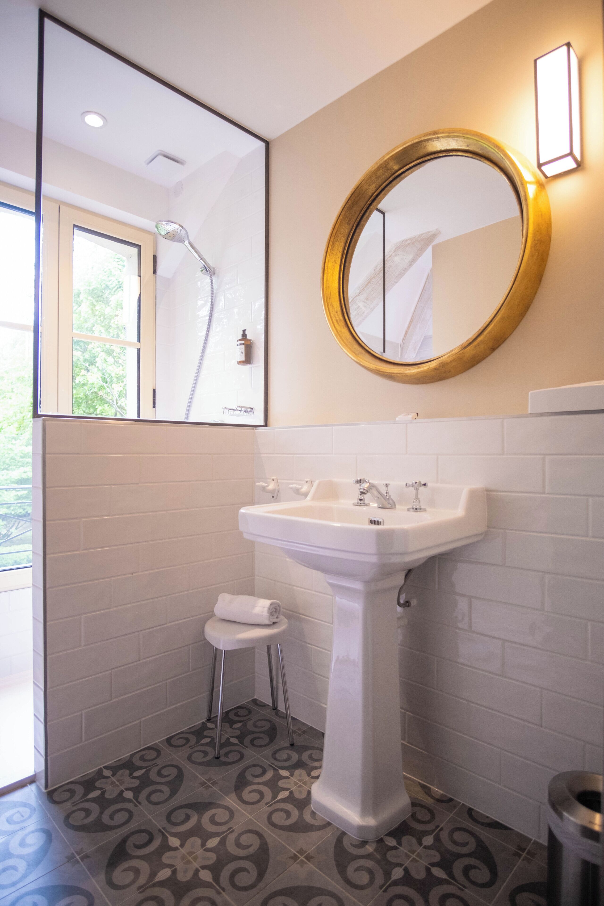 A bathroom with a white sink, a mirror with a gold frame, a shower, and patterned floor tiles.