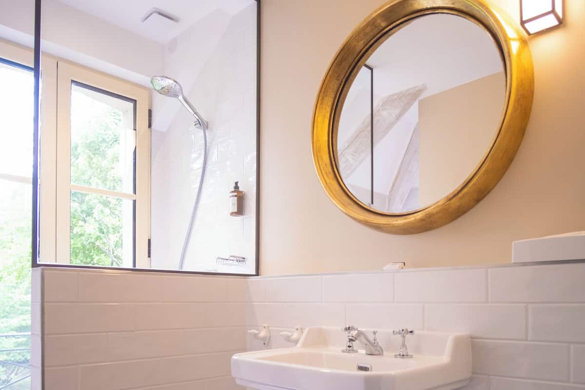 A bathroom with a white sink, a mirror with a gold frame, a shower, and patterned floor tiles.
