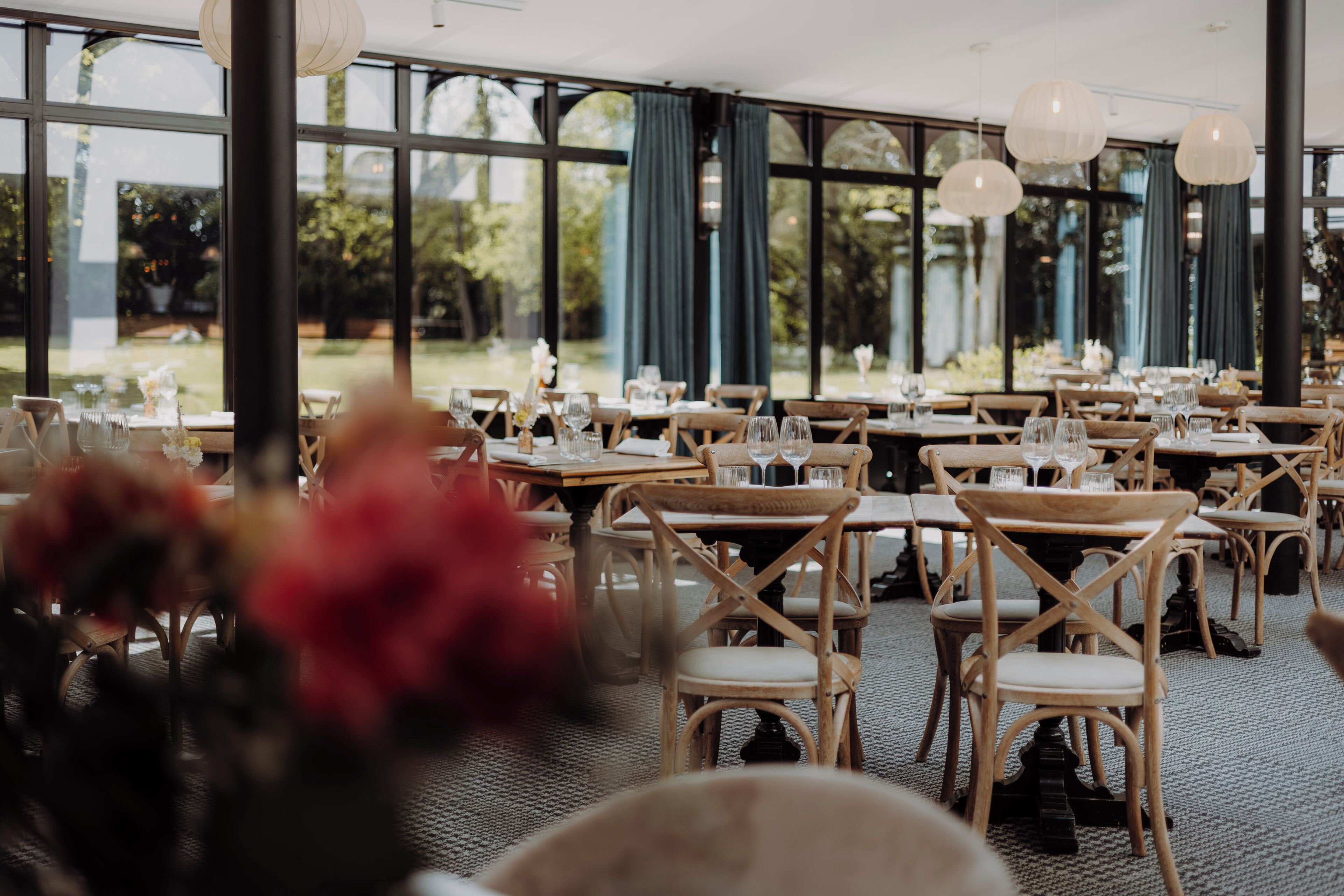 A restaurant with tables set for dining, large windows, and hanging light fixtures.